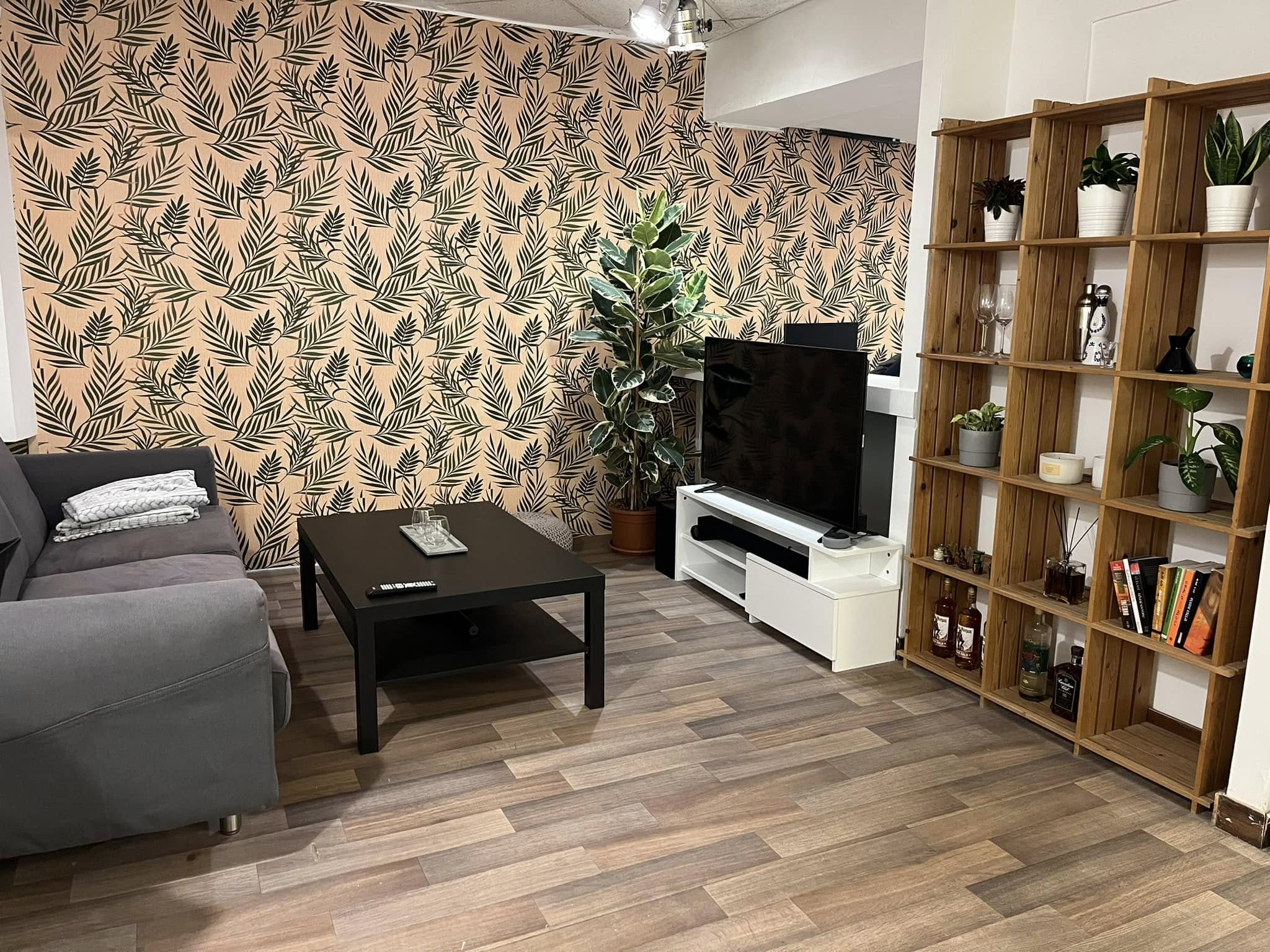 Living room with a grey sofa, low coffee table, botanical feature wall, a large plant and open wooden shelving
