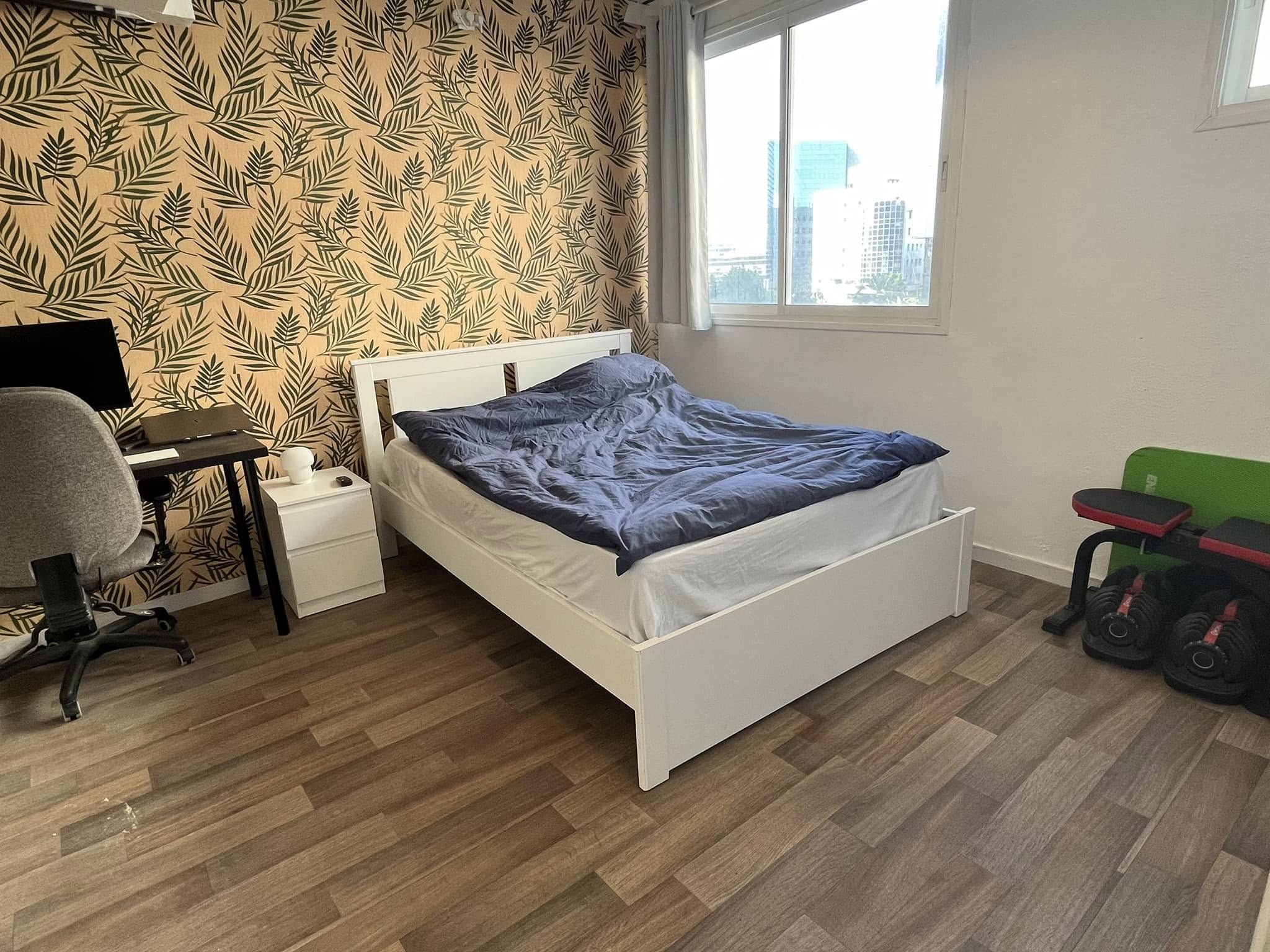 Bedroom with a double bed, botanical wallpaper, a desk workspace and a window looking out over the city